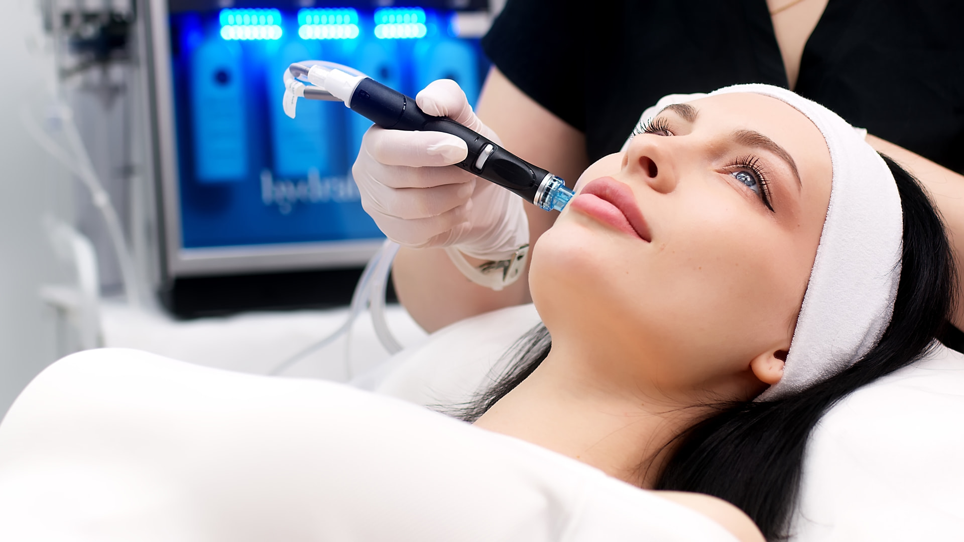 HydraFacial Syndeo Anwendung im Gesicht mit Behandlungsgerät im Hintergrund